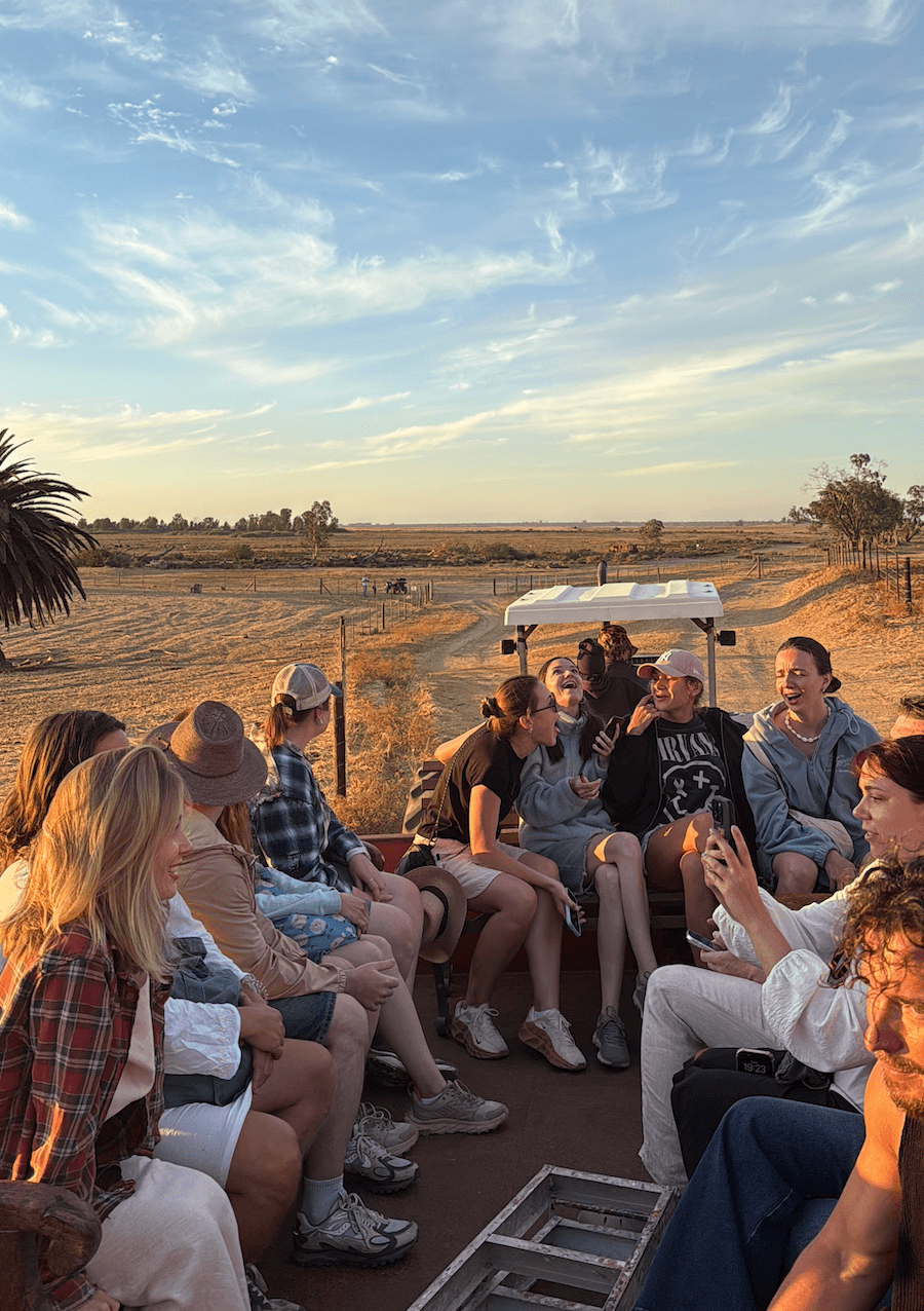 Group of friends laughing and talking in an open trailer during a sunset farm tour.