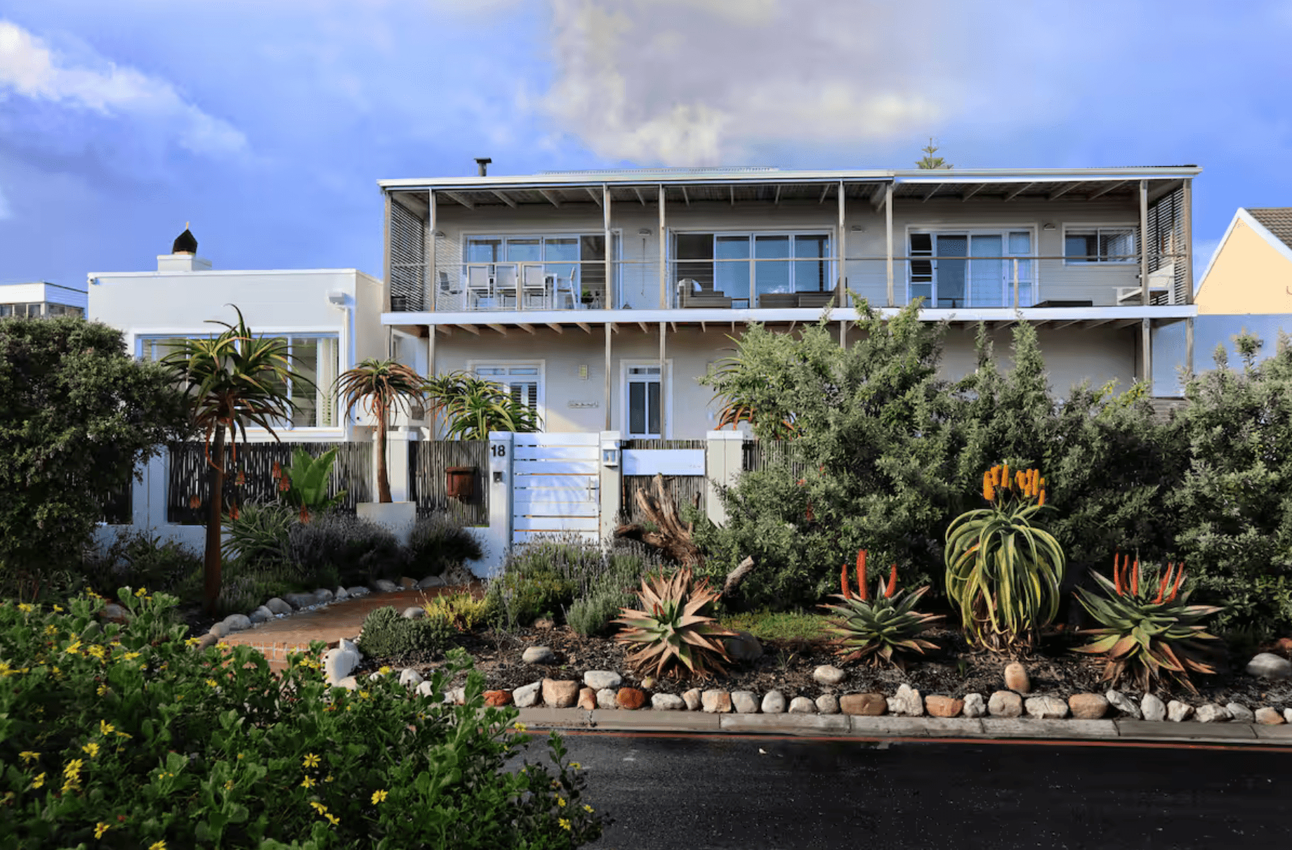 Modern two-story house with a large balcony overlooking a lush garden filled with various succulents.