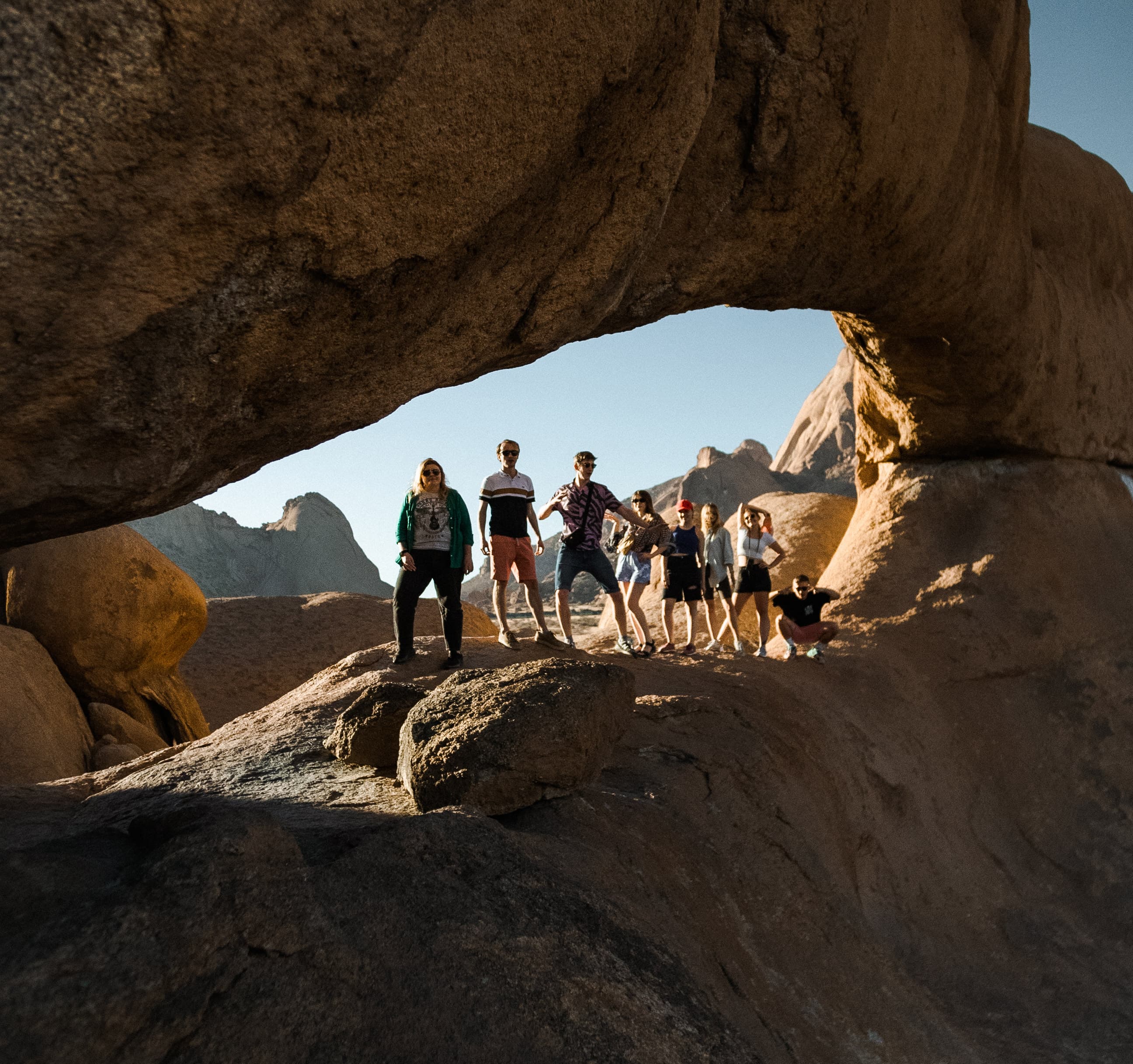 A group of people posing under a massive natural rock arch in a desert landscape.
