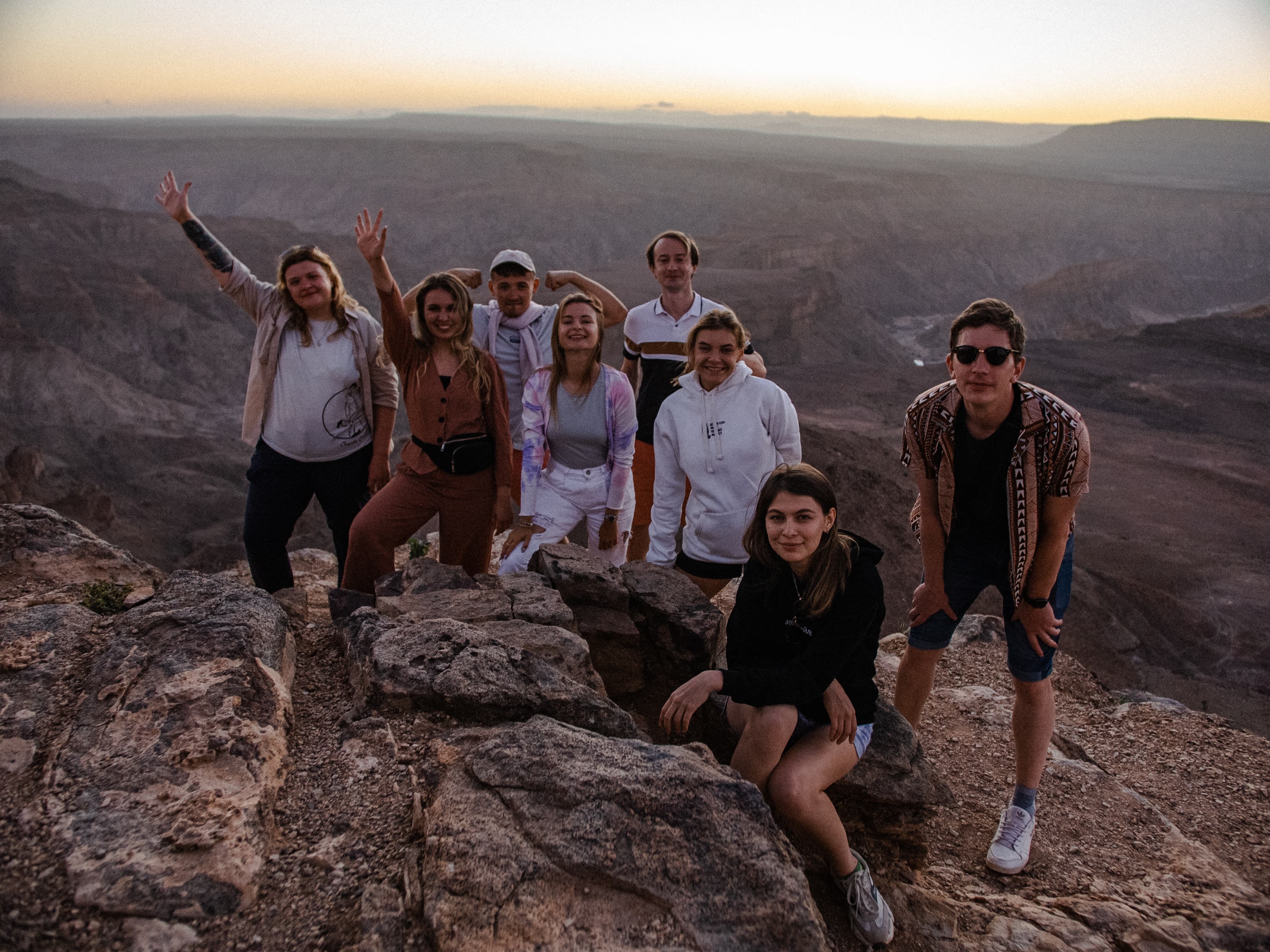 Group of friends posing on a rocky cliff overlooking a vast canyon at sunset.