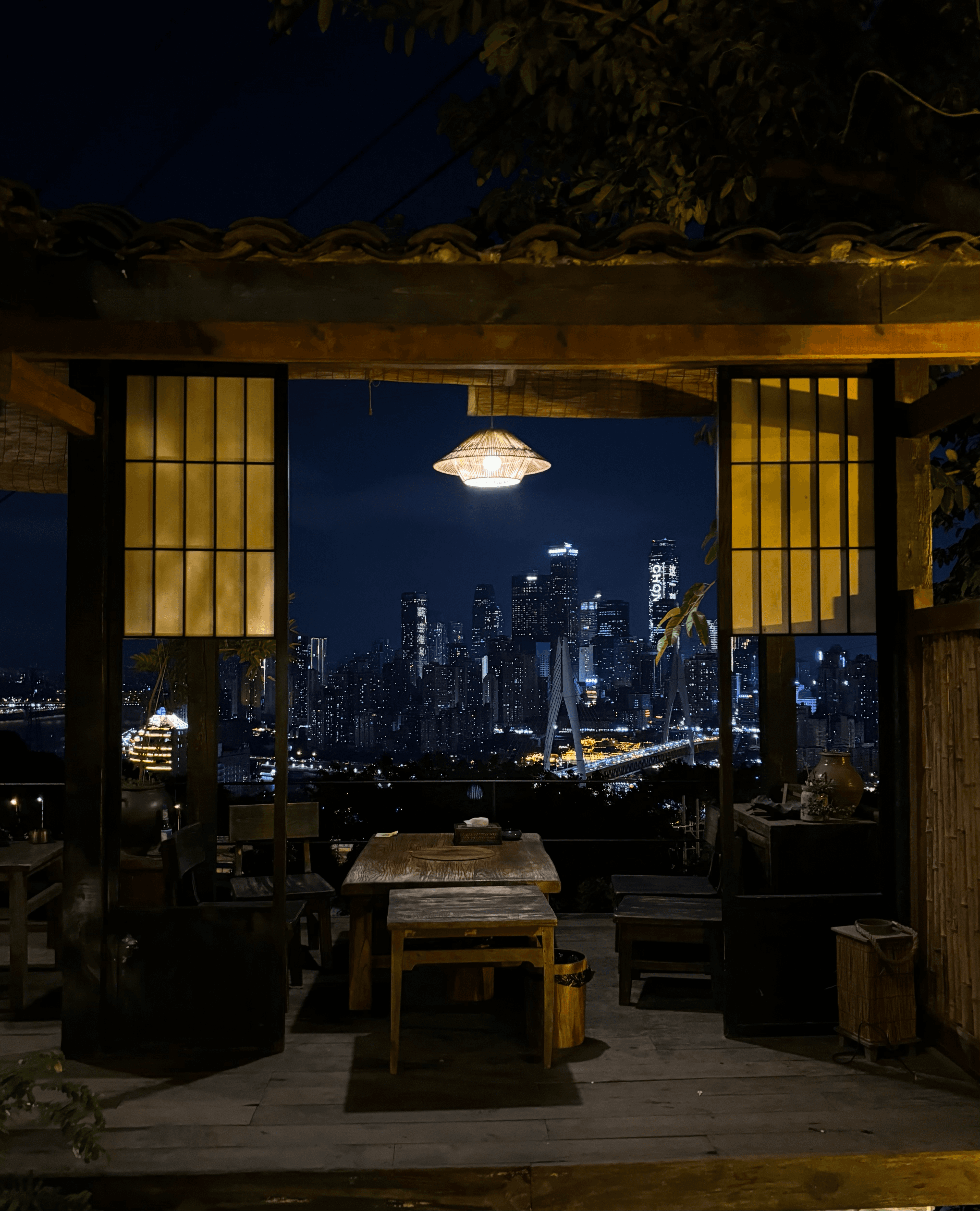 Traditional wooden balcony with a table overlooking a vibrant, illuminated city skyline at night.